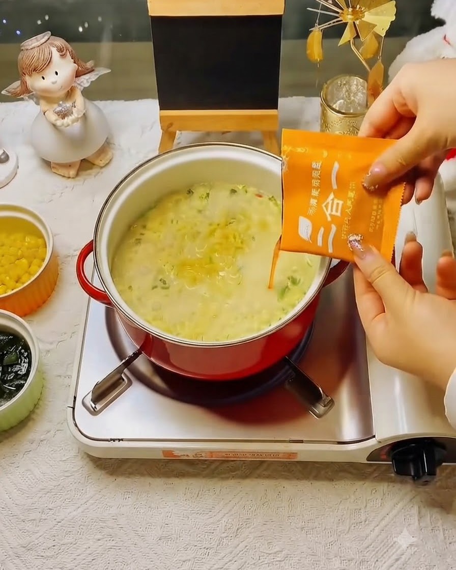 Ein oranges Suppen-Gewürzpäckchen wird in den köchelnden Topf mit Nudeln geschüttet.