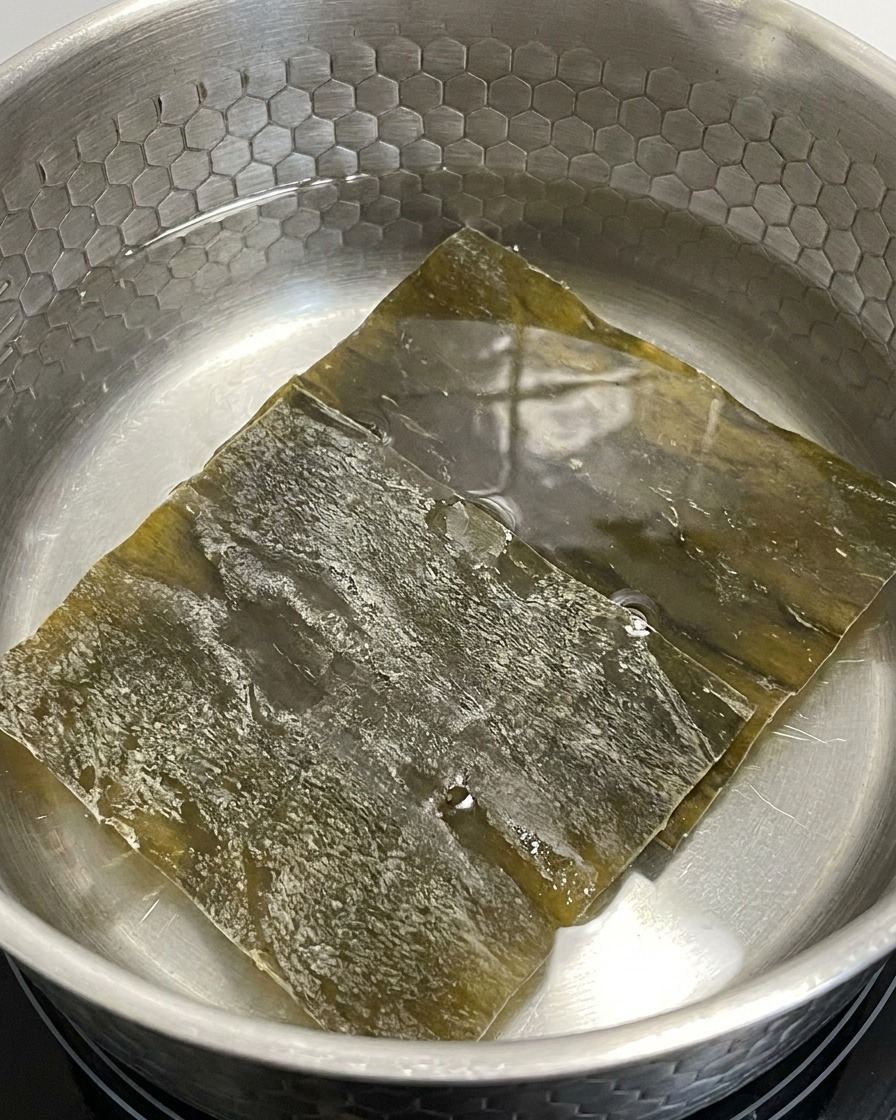 Getrocknete Kelp-Stücke weichen in einem Topf mit Wasser bei schwacher Hitze ein.