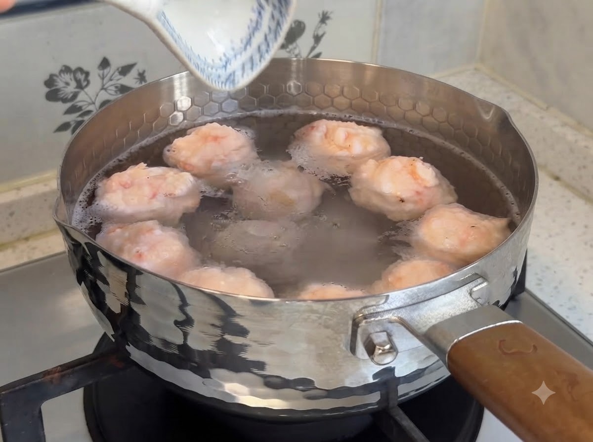 Pralle, hausgemachte Garnelenbällchen köcheln in einem Topf mit warmem Wasser auf dem Herd.
