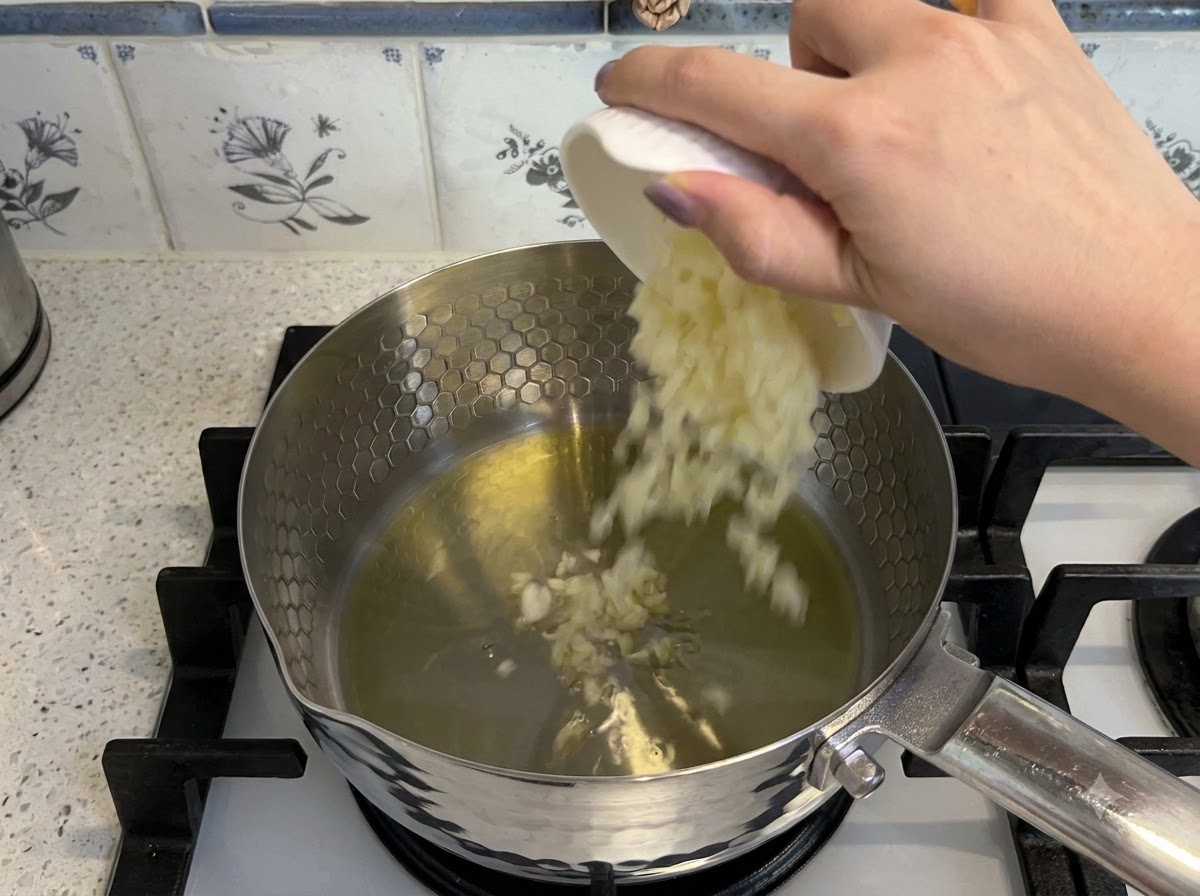 Gehackter Knoblauch und gewürfelte Tomaten werden in heißes Öl in einem Topf zum Anbraten gegeben.