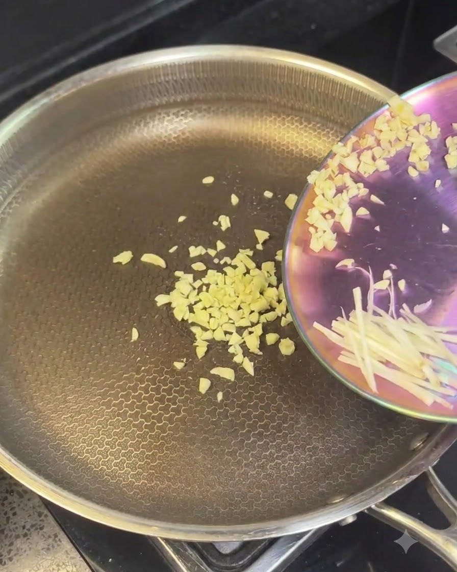 Gehackter Knoblauch und geschnittene Zwiebeln werden in eine heiße Edelstahlpfanne gegeben.