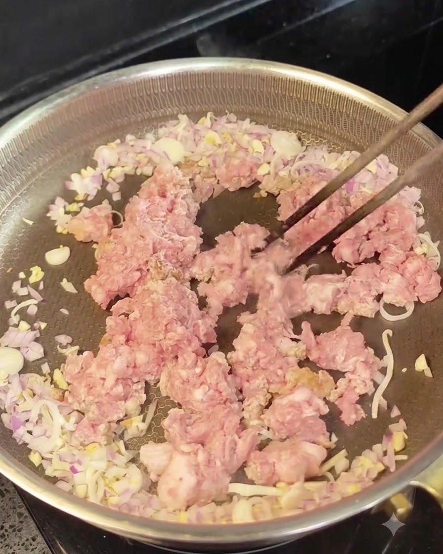 Rohes Hackfleisch in der Mitte einer Pfanne, umgeben von angebratenen Zwiebeln und Knoblauch.
