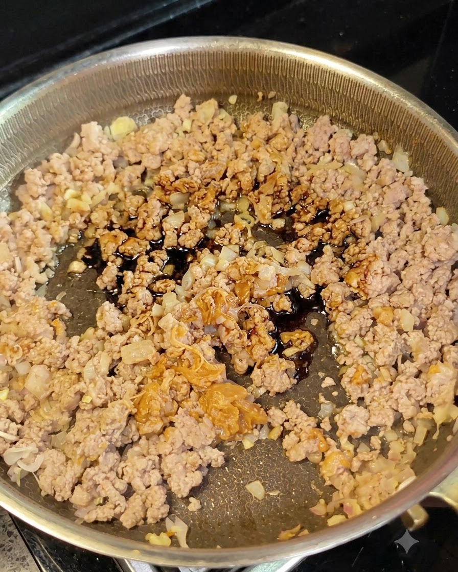 Dunkle Sojasauce wird mit einem Löffel auf das Hackfleisch und die Zwiebeln in der Pfanne gegossen.