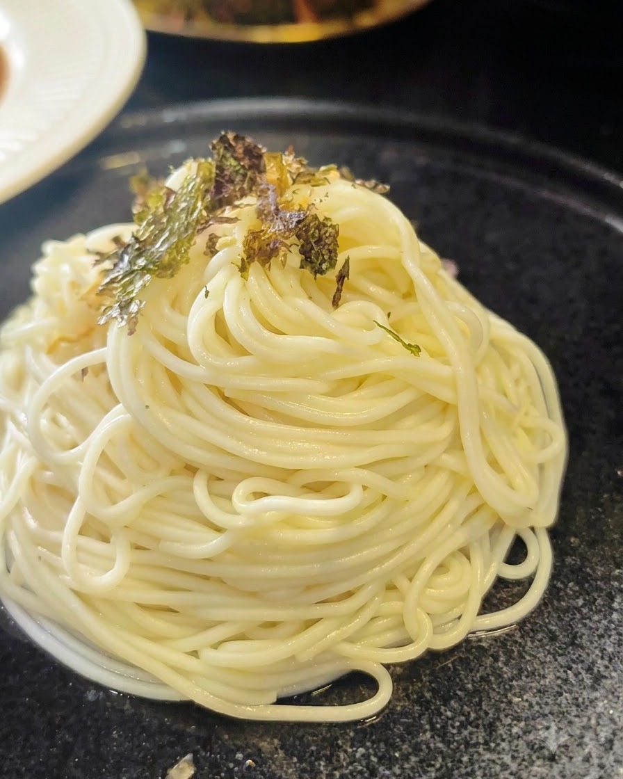 Zerdrückte getrocknete Algenflocken werden über einen ordentlichen Spiralteller mit gekochten Ramen-Nudeln gestreut.