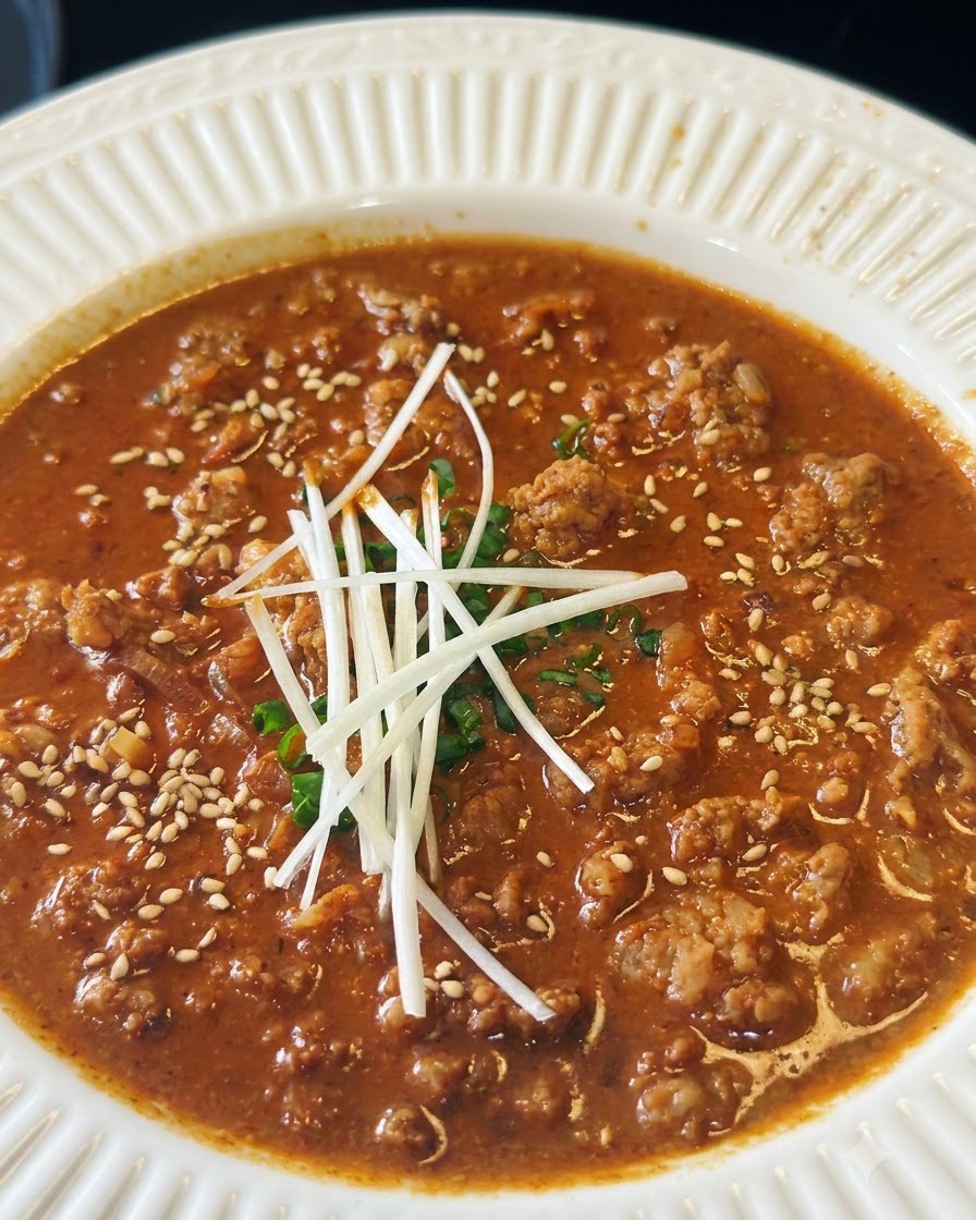 Geröstete weiße Sesamsamen werden über eine Schüssel mit herzhafter Fleischsauce gestreut, die mit Lauchzwiebeln garniert ist.
