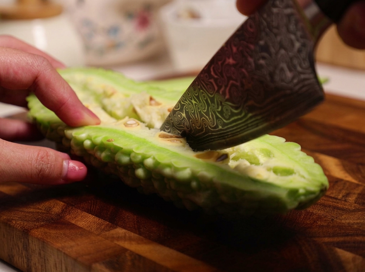 Mit einem Messer werden das schwammige weiße Innere und die Kerne aus der halbierten, rohen Bittermelone gekratzt.