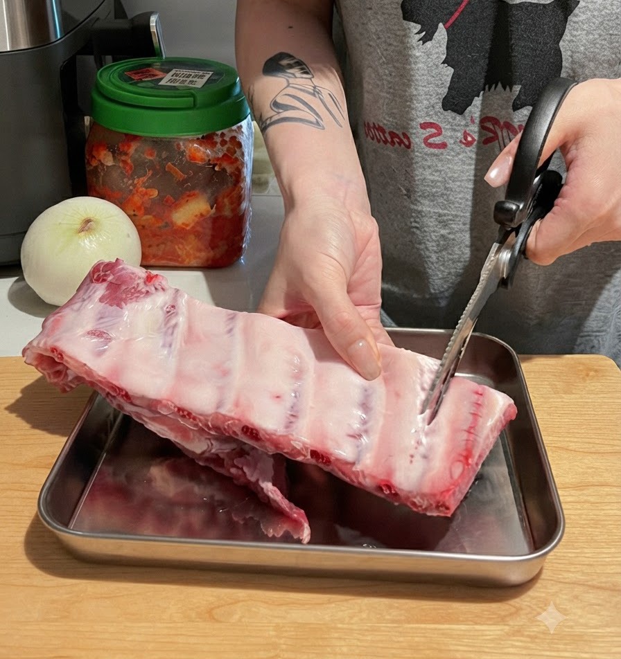 Hände schneiden mit einer Küchenschere einen großen Strang rohe Schweinerippchen auf einem Holzschneidebrett in einzelne Stücke.