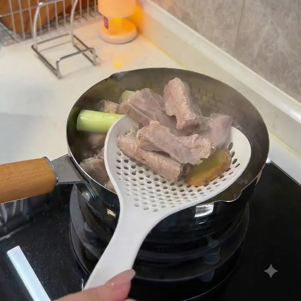 Ein weißer Schaumlöffel hebt blanchierte, undurchsichtige Schweinerippchen und Ingwerscheiben aus kochendem Wasser.