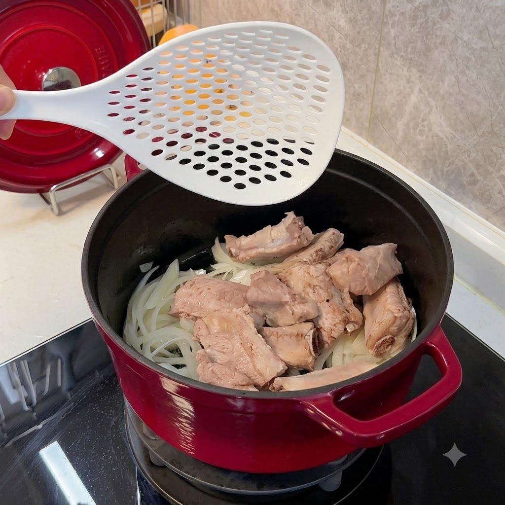 Blanchierte Schweinerippchen werden mit einem weißen Schaumlöffel in einen roten Topf auf ein Bett aus weichen Zwiebeln gelegt.