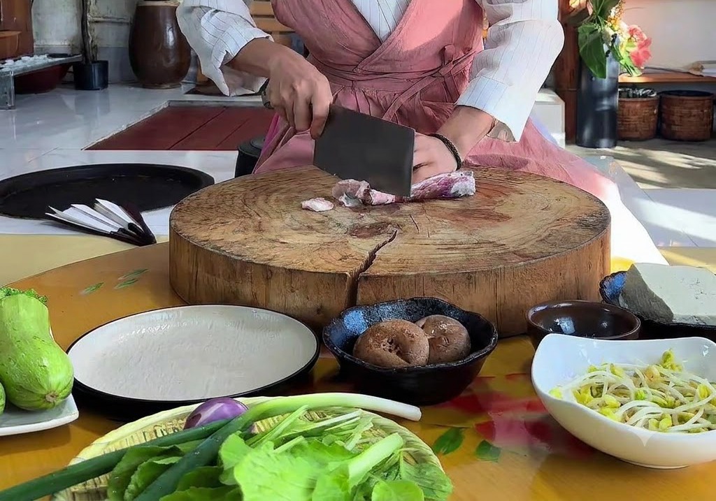 Hände schneiden rohen Schweinebauch mit einem Beil auf einem großen runden Holzschneidebrett.