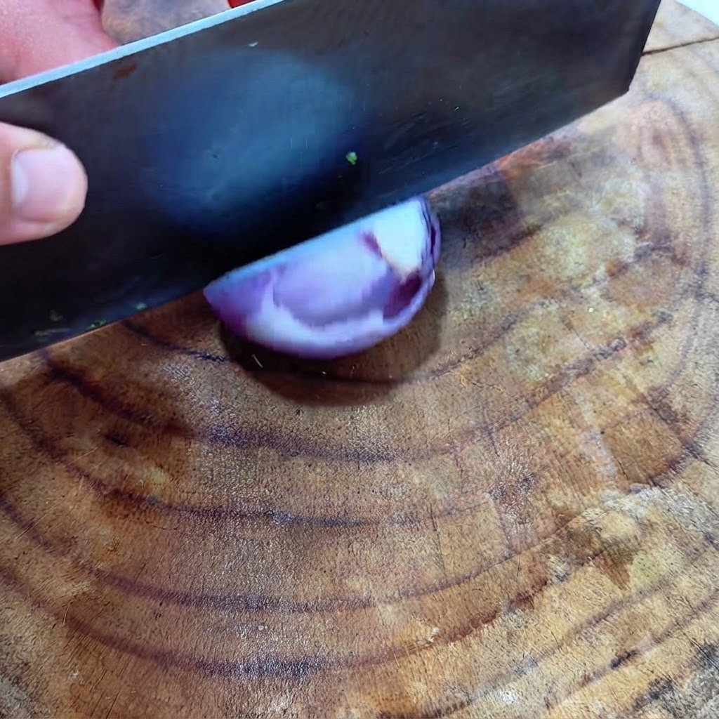 Ein großes Beil würfelt eine halbe rote Zwiebel auf einer Holzoberfläche.