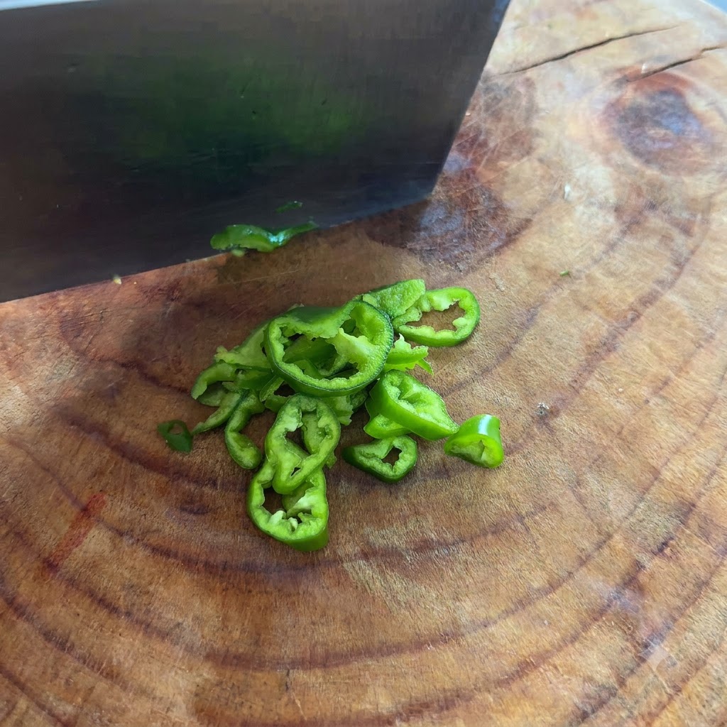 Grüne Chilischoten werden mit einem Messer auf einem Schneidebrett in dünne Ringe geschnitten.