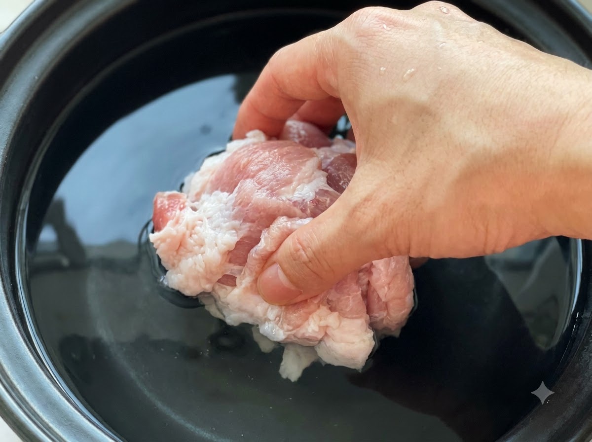 Rohe Schweinefleischstücke werden in einen Topf mit kaltem Wasser und Sojabohnenpaste gegeben.