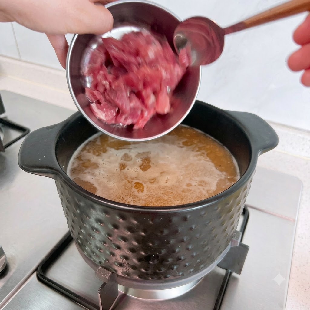 Rohe Schweinefleischstücke werden aus einer Metallschüssel in einen Topf mit kochender Suppe gegossen.