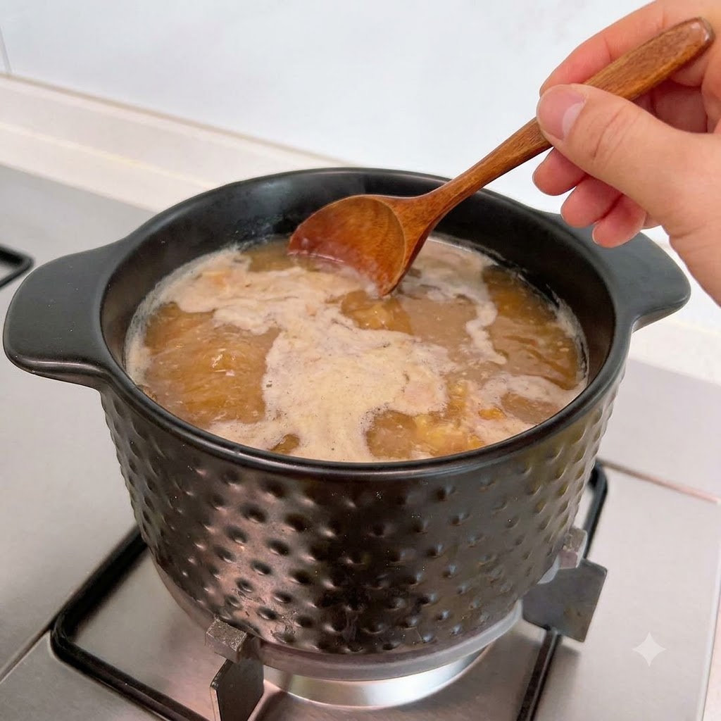 Ein Holzlöffel schöpft Schaum von der Oberfläche der köchelnden Suppe im Topf ab.
