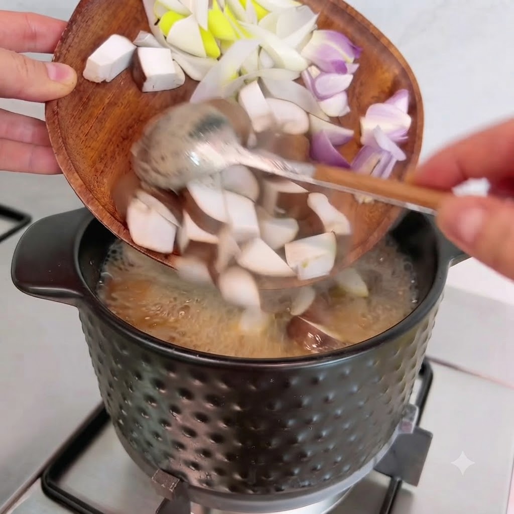 Gewürfelte Shiitake-Pilze, Zwiebeln und Frühlingszwiebeln werden von einem Holzteller in den Topf gekippt.