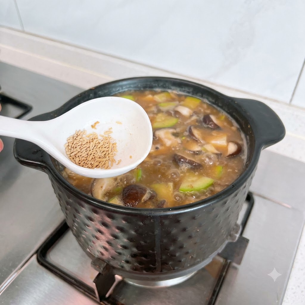 Ein weißer Löffel mit Rinderbrühepulver über einem blubbernden Topf mit Doenjang Jjigae.