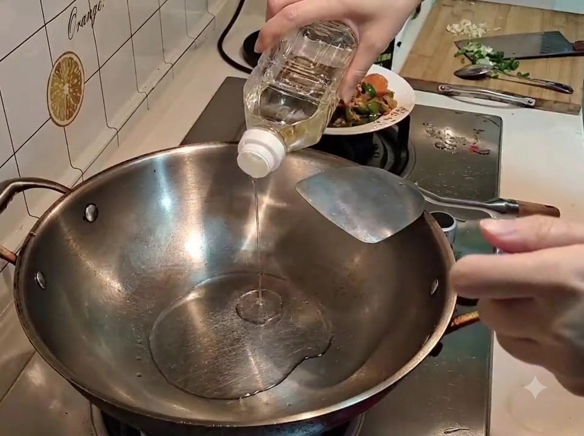 Eine Hand gießt klares Speiseöl aus einer Plastikflasche in einen erhitzten Edelstahlwok.