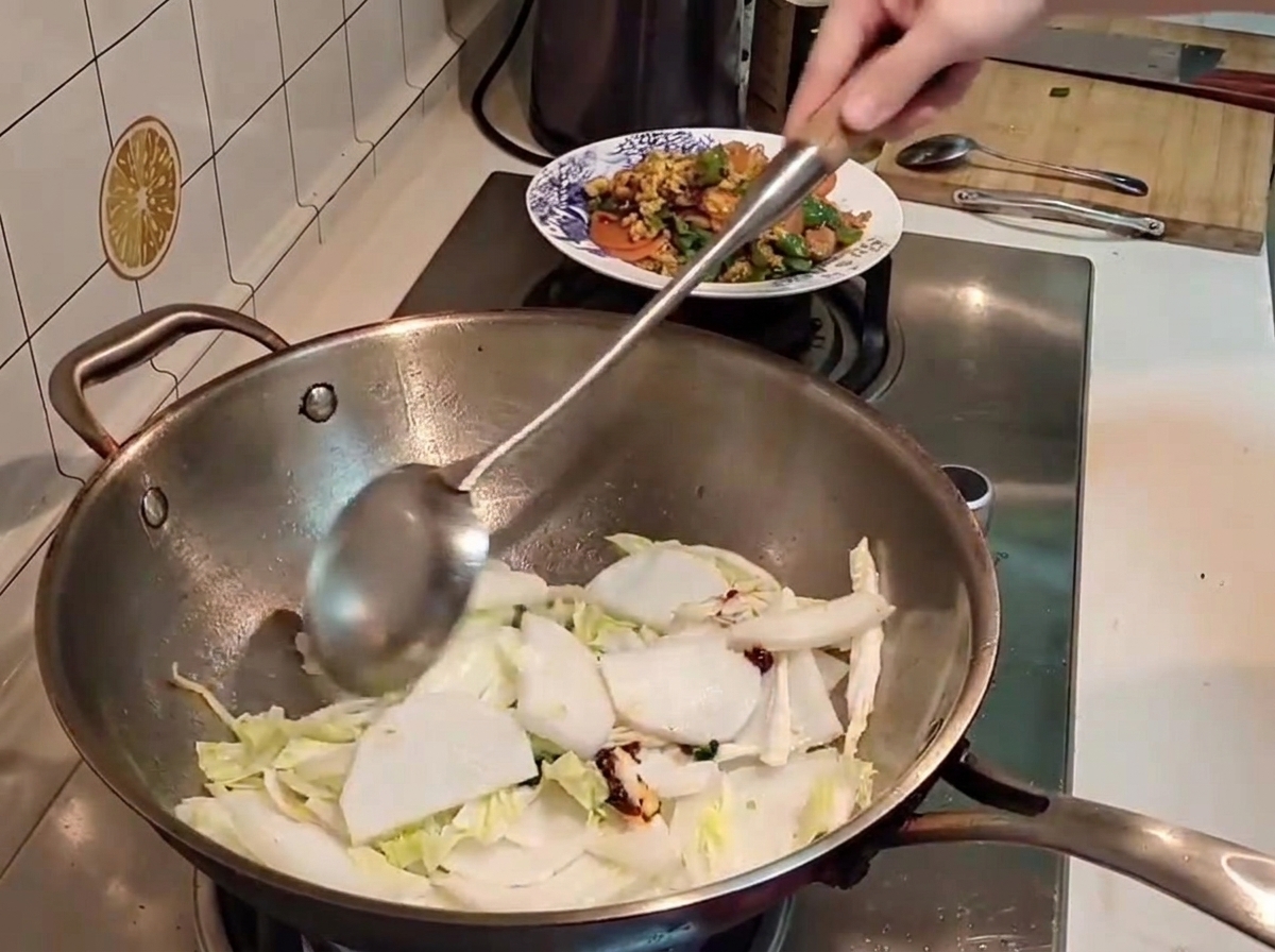Ein Metallpfannenwender wendet Stücke von Chinakohl und weißem Rettich mit roter Chilipaste in einem heißen Wok.