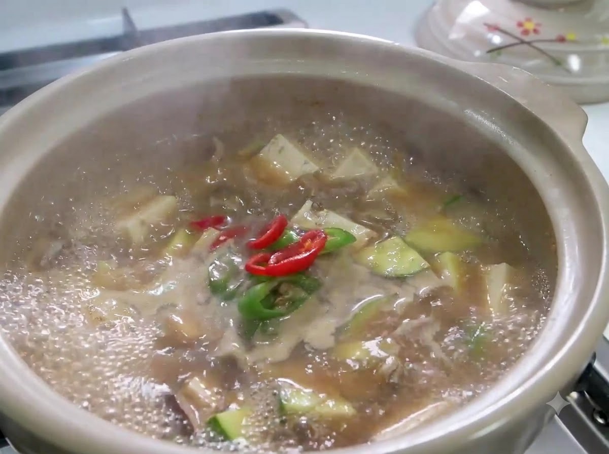 In Scheiben geschnittene rote und grüne Chilischoten sowie Frühlingszwiebeln köcheln in einem sprudelnden Topf mit Doenjang Jjigae.