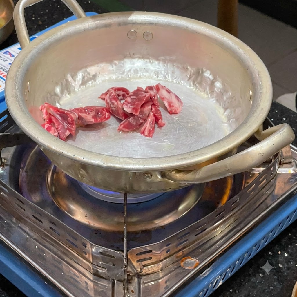 Rohe Rindfleischstücke werden in einem kleinen Metalltopf über einem brennenden tragbaren Gaskocher angebraten.