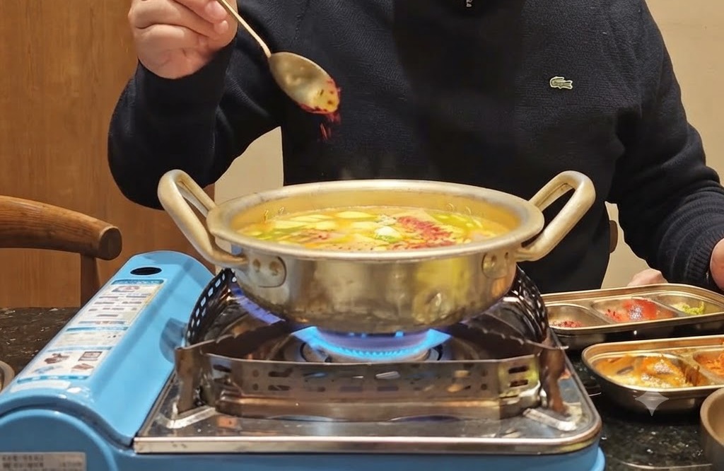 Ein Löffel rotes Chilipulver wird über einen blubbernden Topf gestreut, der mit Gemüse und Brühe gefüllt ist.