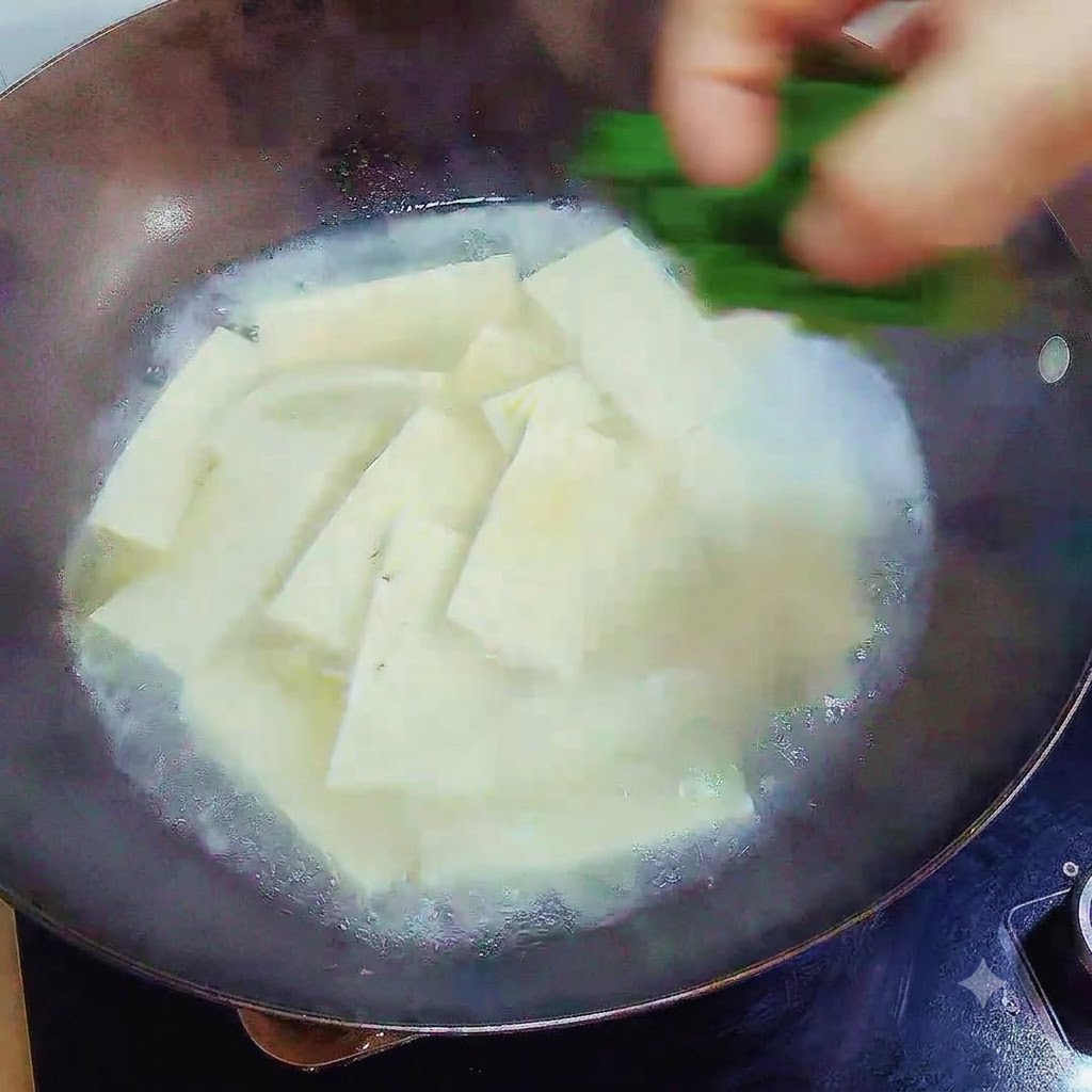 Eine Hand lässt gehackte grüne Frühlingszwiebeln über die fertige Tofusuppe im Wok fallen.