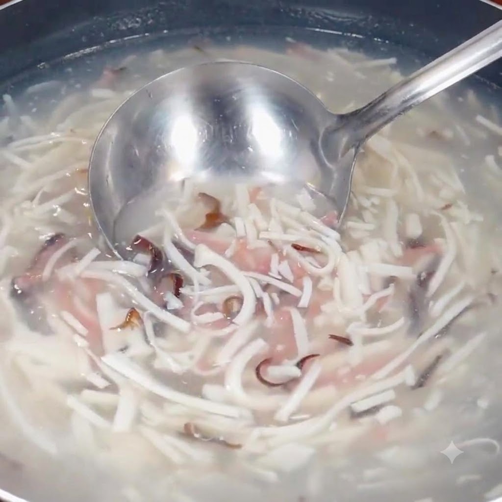 Eine Kelle schöpft die köchelnde Suppe mit den feinen Zutaten aus dem Topf.