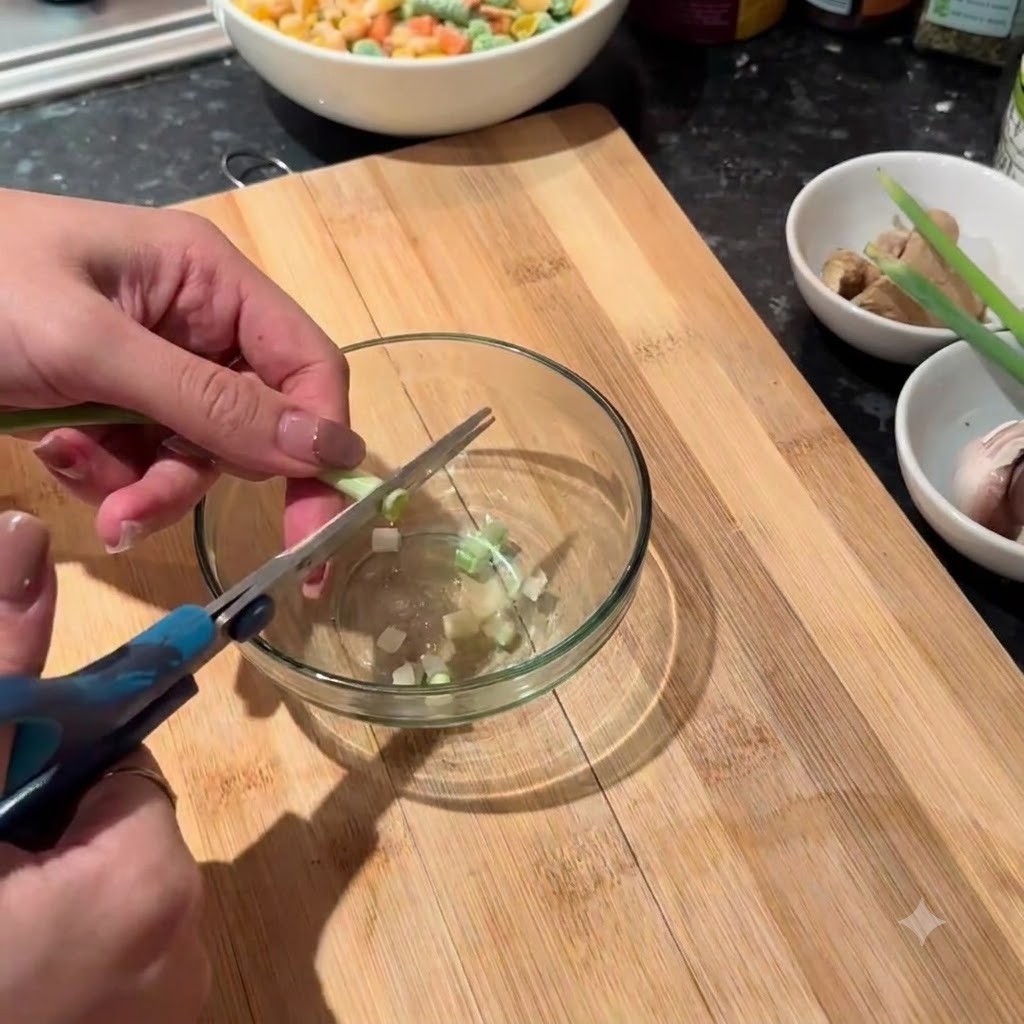 Frische Lauchzwiebelstängel werden mit einer Schere in kleine Stücke in eine Glas schüssel geschnitten.
