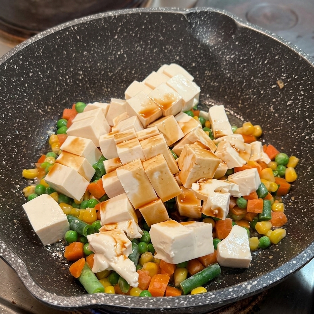 Sojasauce wird über weiche Tofuwürfel und Gemüsemischung in einer Pfanne verteilt.