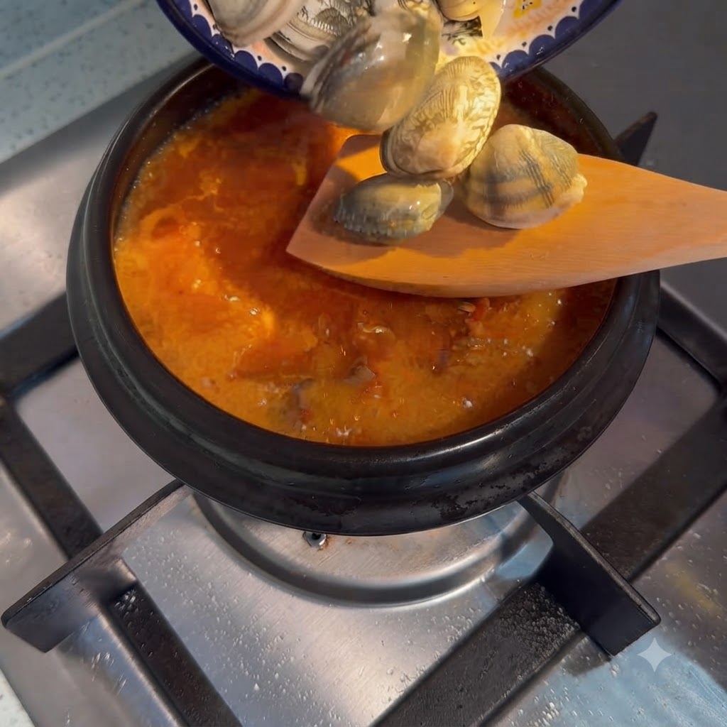 Frische Venusmuscheln werden von einem kleinen Teller in einen kochenden Topf mit koreanischem Seidentofu-Eintopf gegeben.
