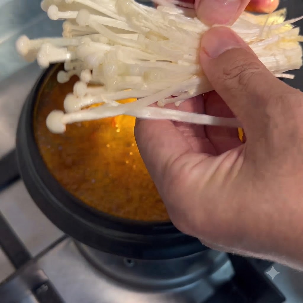 Enoki-Pilze werden mit der Hand gehalten und in den köchelnden Suppentopf getaucht.