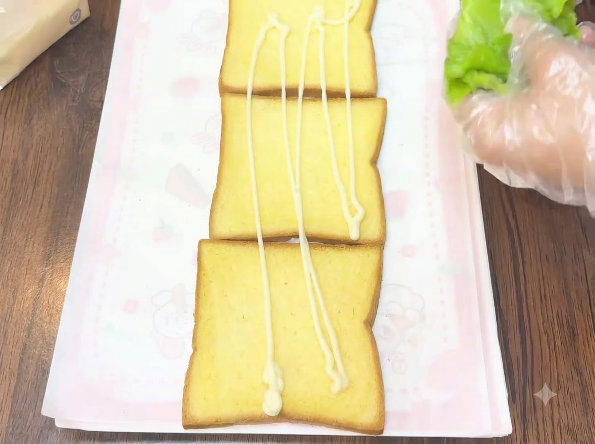Eine handschuhbekleidete Hand legt frische grüne Salatblätter auf eine Toastscheibe mit Dressing.