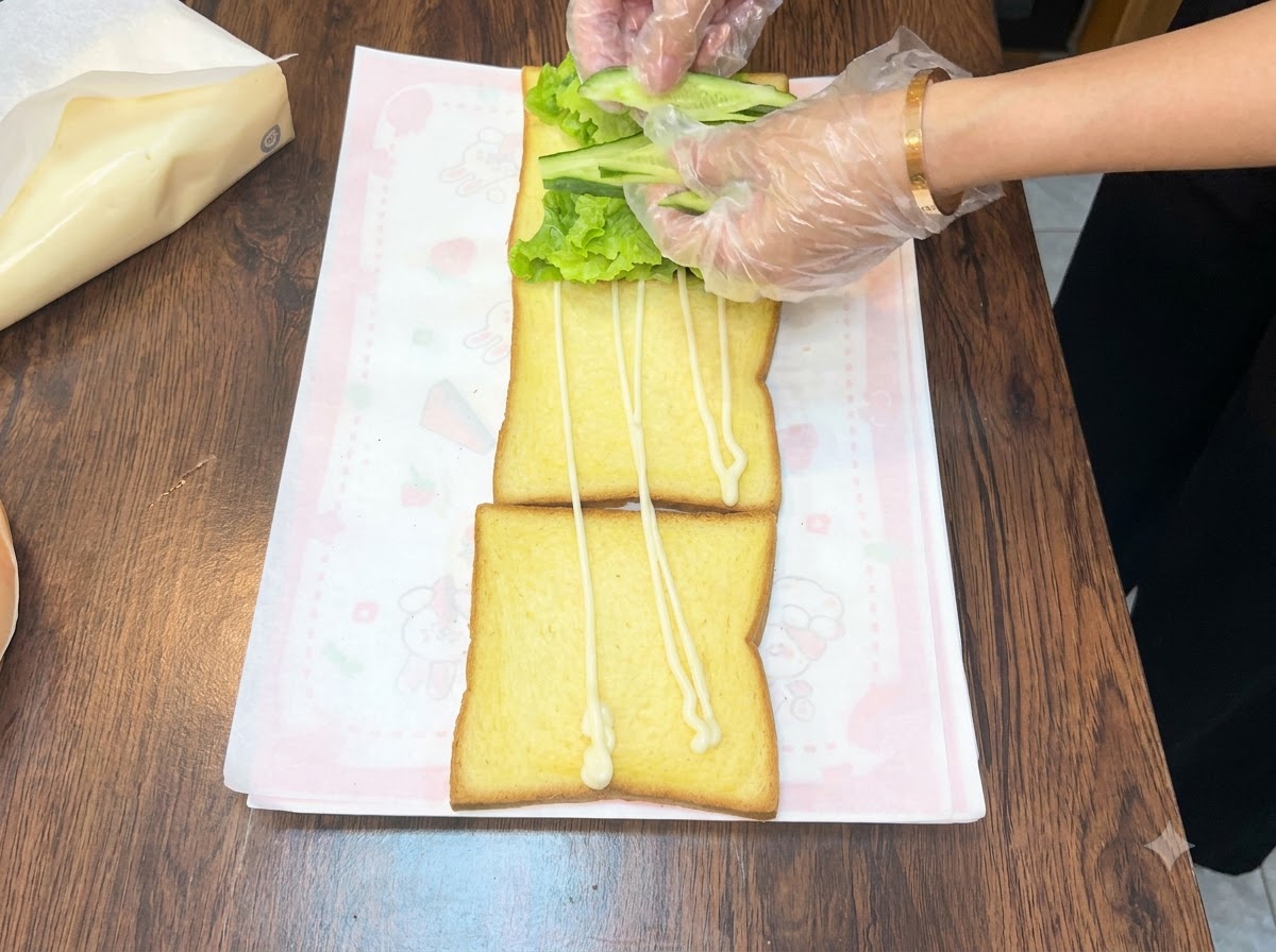 Hände ordnen frische grüne Gurkenscheiben über einem Salatbett auf einem Toaststück an.