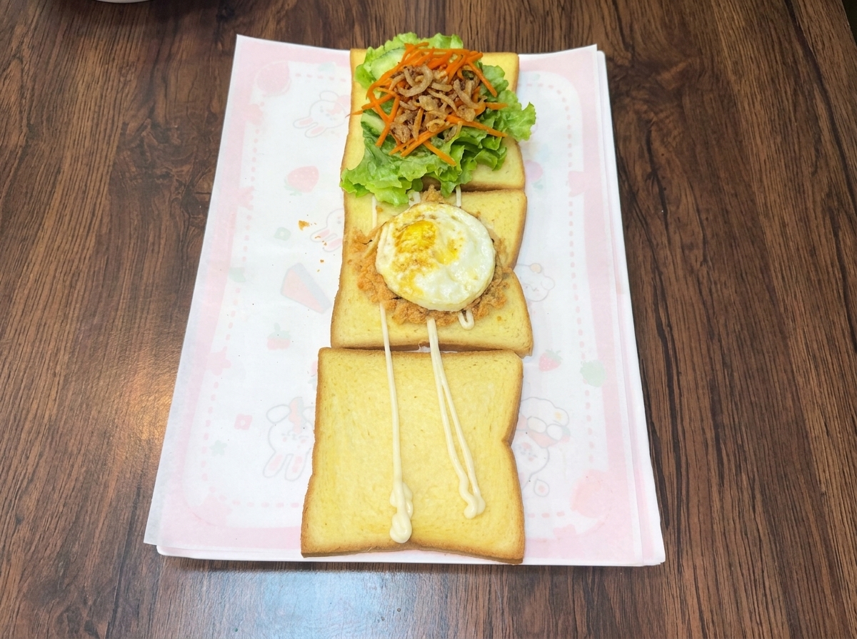 Ein frisch gebratenes Ei auf einer Schicht aus herzhaftem Fleischfloss und Algenkrumen auf einer Toastscheibe.