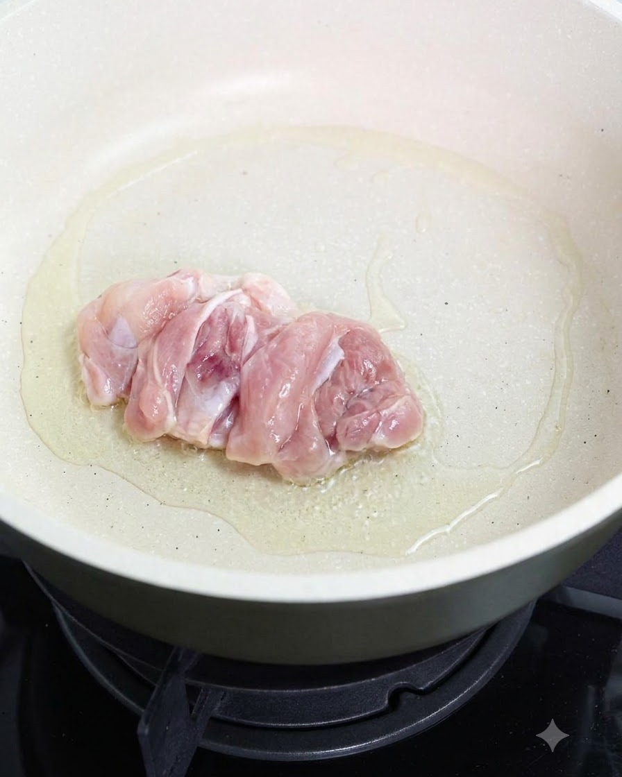 Ein roher Hähnchenschenkel brät mit der Hautseite nach unten in einer geölten Pfanne.