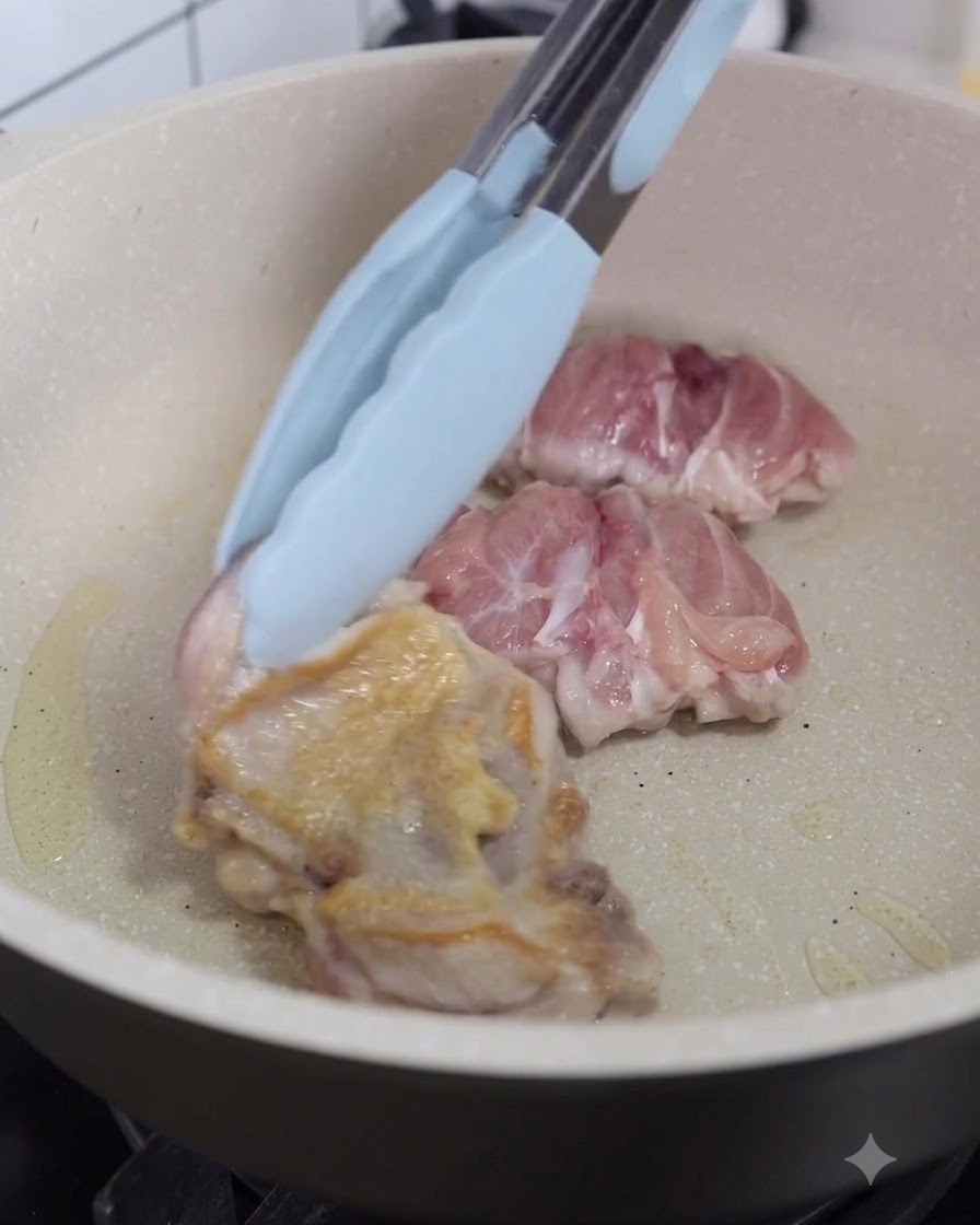 Hähnchenstücke werden in der Pfanne mit einer Küchenzange umgedreht.