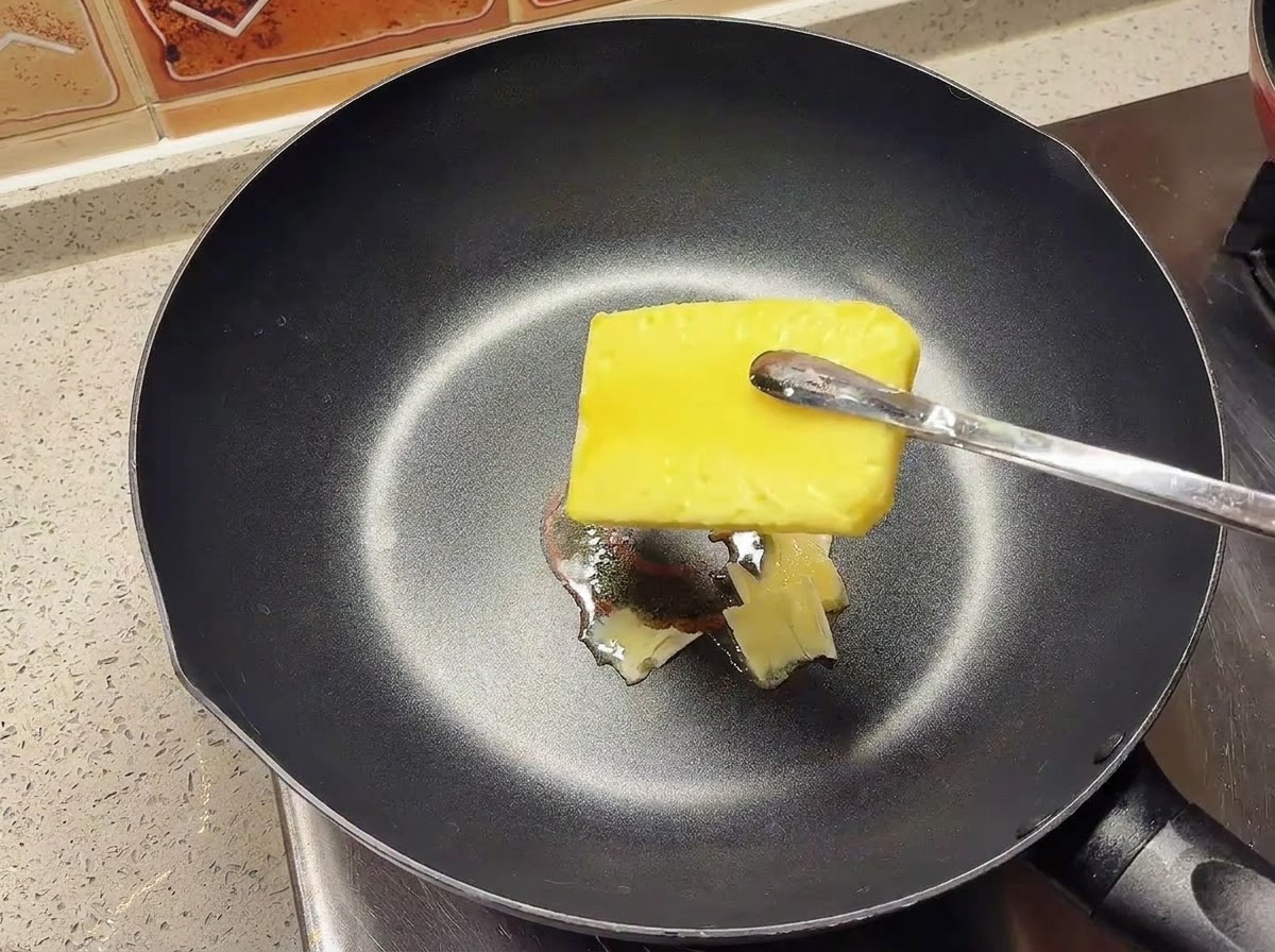 Ein Stück gelbe Butter schmilzt in einer heißen, schwarzen Pfanne.