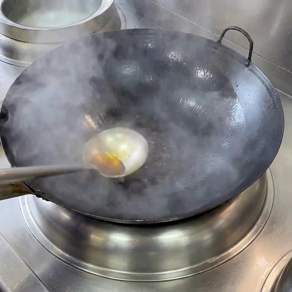 Ein rauchender Gusseisen-Wok mit heißem Öl wird auf dem Herd erhitzt.