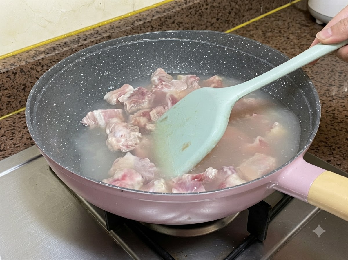 Schweinerippchen kochen in Wasser in einer Pfanne, während sie mit einem hellblauen Silikonspatel umgerührt werden.