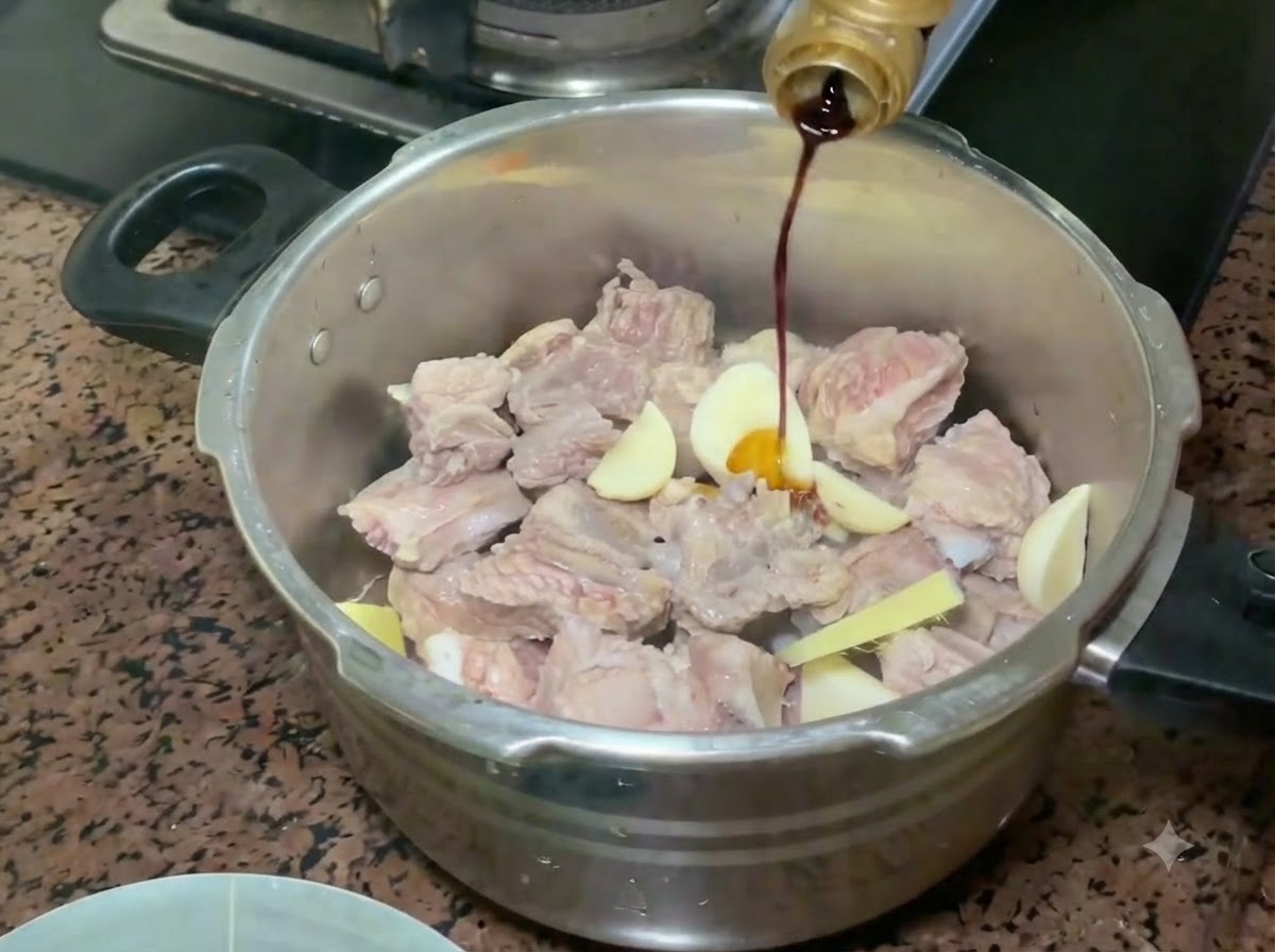 Helle Sojasauce wird aus einer Flasche über die Schweinerippchen und das Würzgemüse im Schnellkochtopf gegossen.
