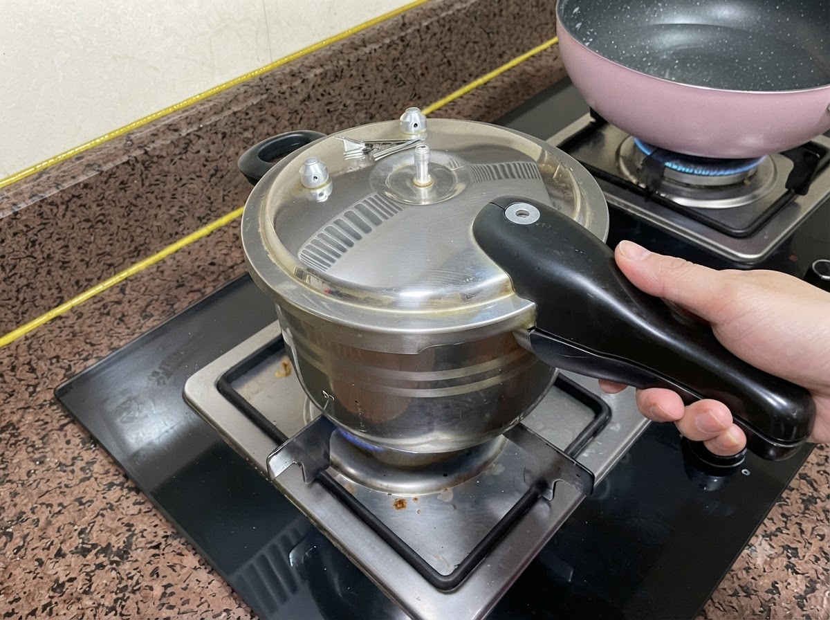 Ein Schnellkochtopfdeckel auf einer Herdplatte mit einer Hand am Griff.