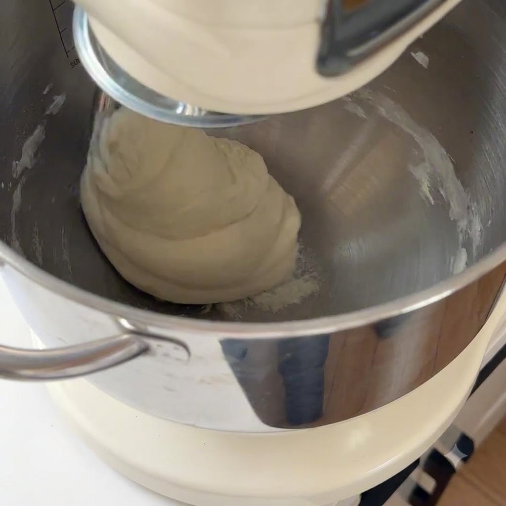 Ein glatter Pizzateig wird in der Schüssel einer Küchenmaschine geknetet.