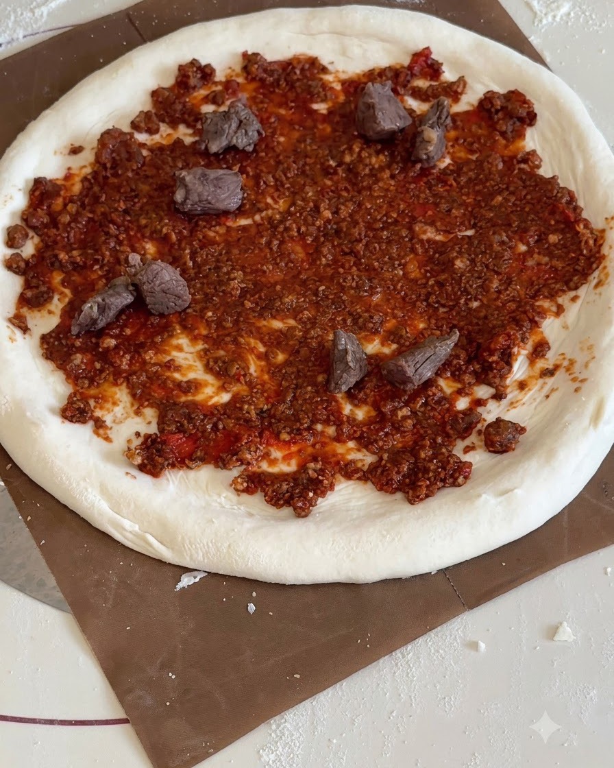Dreieckige Stücke gelber Ananas und Rindfleischwürfel sind auf der Pizza mit roter Soße verteilt.
