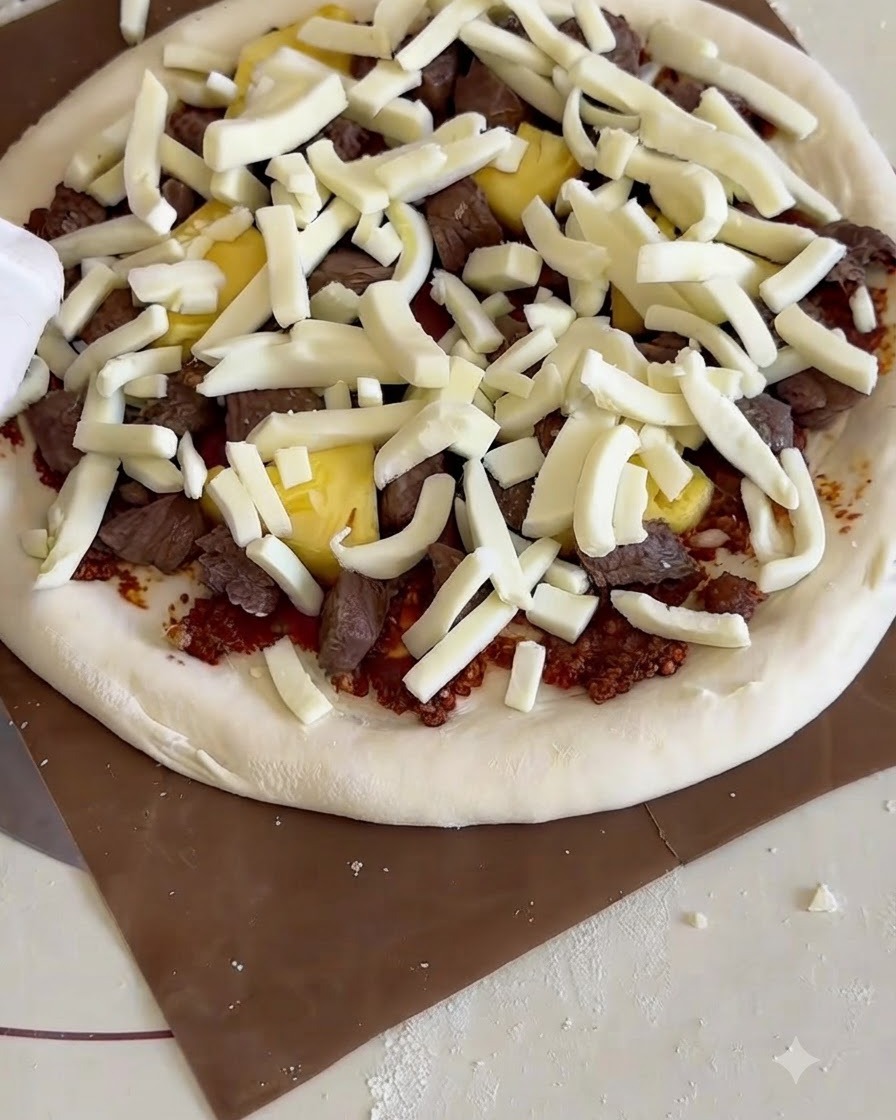 Eine fertig belegte, rohe Pizza wird von einem Holzschieber in einen Tisch-Pizzaofen mit Pizzastein geschoben.