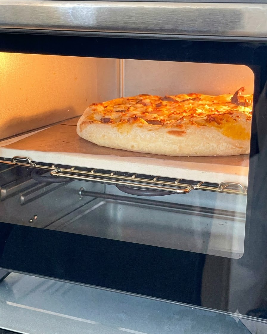 Eine goldbraun gebackene Pizza mit geschmolzenem Käse auf einem Pizzastein in einem kleinen Ofen.