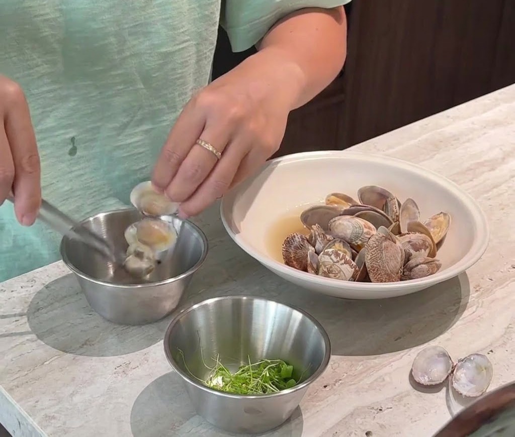 Eine Person löst sorgfältig gekochtes Muschelfleisch aus den Schalen und legt es in eine kleine Metallschüssel.