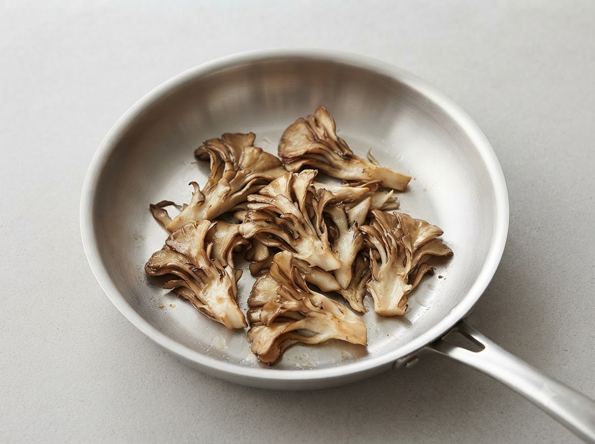 In Stücke gerissene Maitake-Pilze bräunen in einer sauberen Pfanne aus Edelstahl.