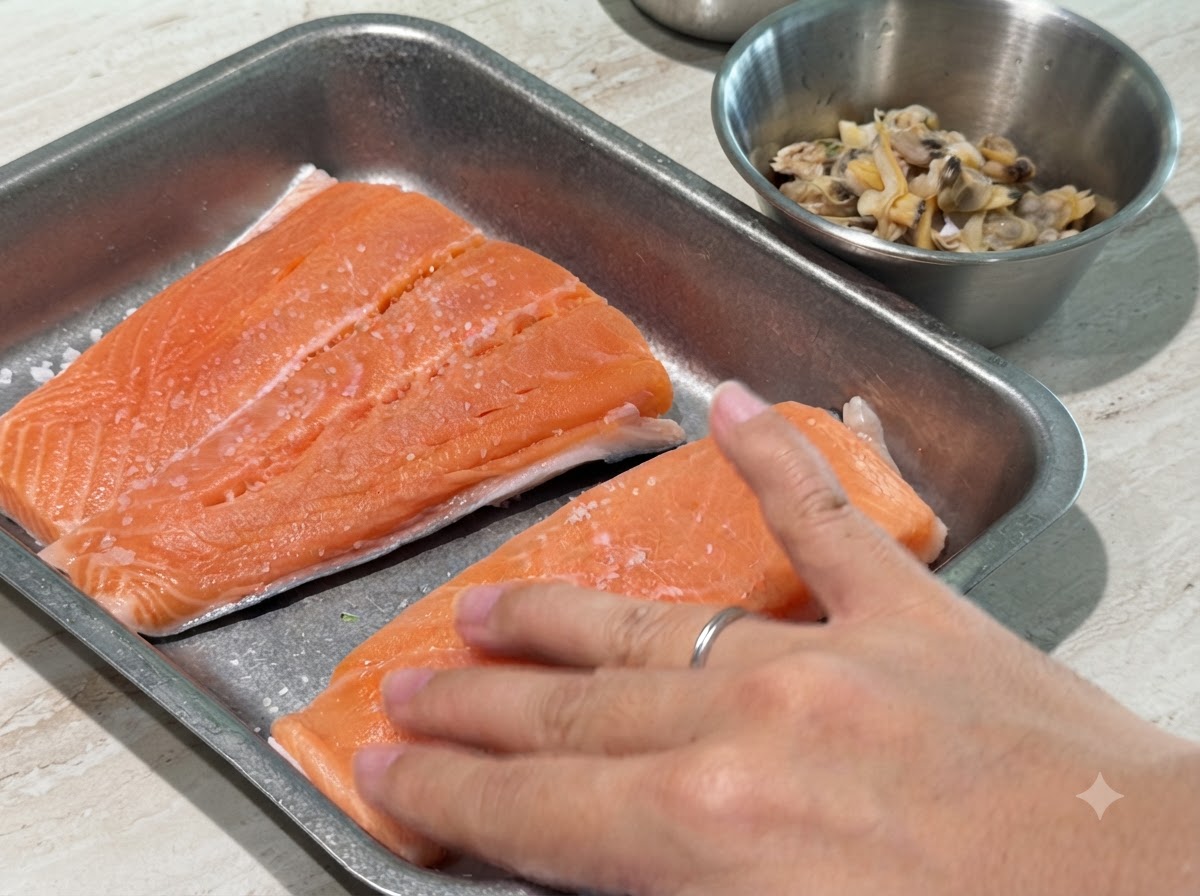 Eine Hand drückt leicht Salz und schwarzen Pfeffer auf rohe Lachsfilets.