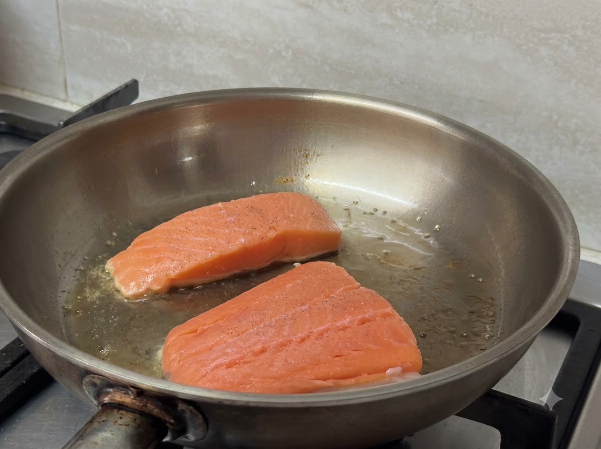 Zwei Lachsfilets braten zischend und bräunend in einer heißen Pfanne.